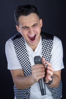 Young black-haired man dressed in black and white performs singing to microphone