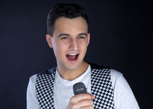 Young black-haired man dressed in black and white performs singing to microphone