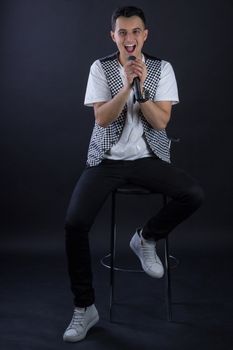 Young black-haired man dressed in black and white poses singing to microphone