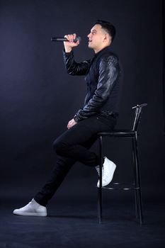 Young black-haired man dressed in black and white poses singing to microphone