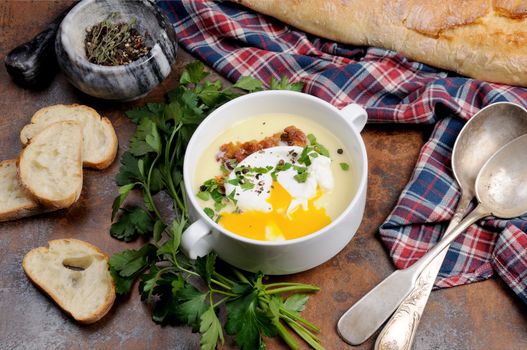 Garlic potato cream soup with bacon and poached eggs, herbs, spices