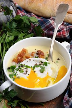 Garlic potato cream soup with bacon and poached eggs, herbs, spices
