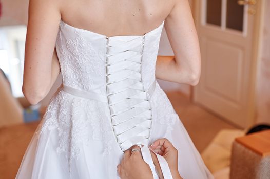 bridesmaid helping to dress the bride in a wedding morning.