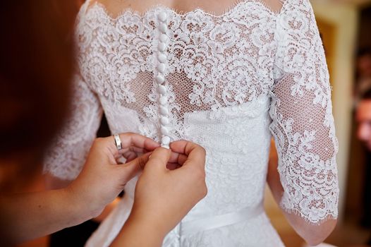 bridesmaid helping to dress the bride in a wedding morning.