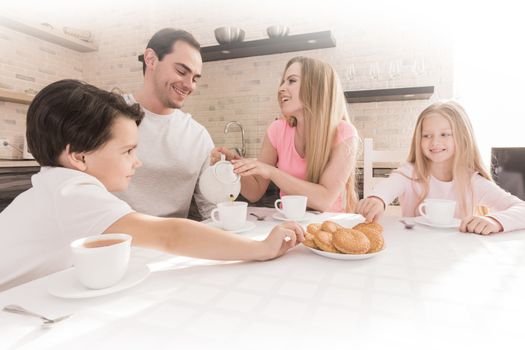 Family eating cookies with tea in the kitchen at home