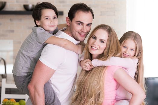 Portrait of happy family, father and mother giving boy and girl piggy back ride at home