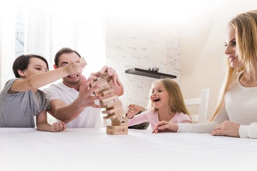 Happy family having fun playing Jenga, tower collapsing