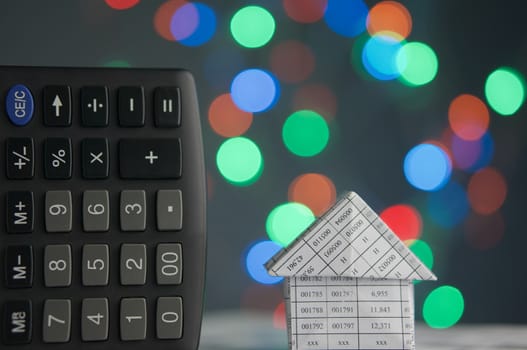 House and calculator have colorful bokeh circle or defocused of glitter at night as background.