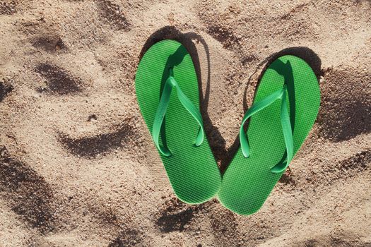 green flip flops in the sand near the sea.