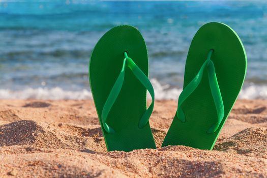 green flip flops in the sand near the sea.