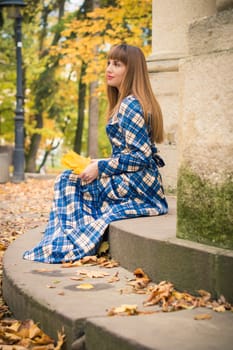 beautiful, dreamy girl with long straight hair in a blue long dress in the park in autumn