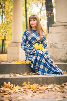 beautiful, dreamy girl with long straight hair in a blue long dress in the park in autumn