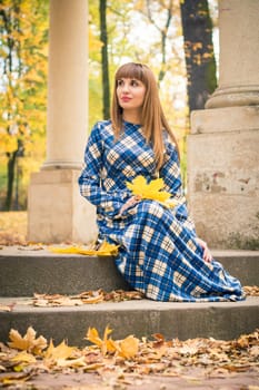 beautiful, dreamy girl with long straight hair in a blue long dress in the park in autumn