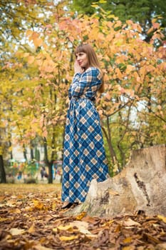 beautiful, dreamy girl with long straight hair in a blue long dress in the park in autumn