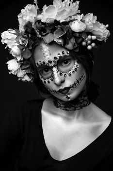 Fashion black and white portrait of a beautiful Halloween model with creative make up,  rhinestones and wreath of flowers on black background