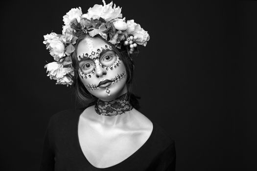 Fashion black and white portrait of a beautiful Halloween model with creative make up,  rhinestones and wreath of flowers on black background