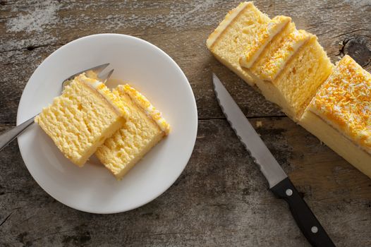 Overhead view of mouth watering yellow cake on round white plate with fork beside knife