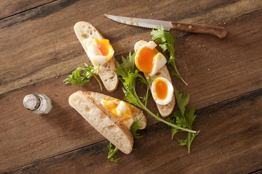 Soft cooked eggs sliced and served on bread beside long stemmed herbs and a serrated knife
