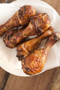 Top down close up on four roasted barbecue drumsticks in white plate with paper towel over wooden table