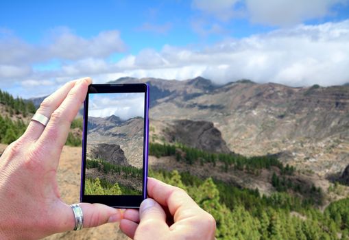 View over the mobile phone display during shooting Gran Canaria mountains. Holding the mobile phone in hands and taking a photo, focused on mobile phone screen.