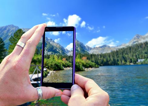 View over the mobile phone display during shooting nature of High Tatras. Holding the mobile phone in hands and taking a photo, focused on mobile phone screen.