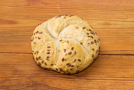 Round wheat sourdough bun, sprinkled with flax and sesame seeds on an old wooden surface
