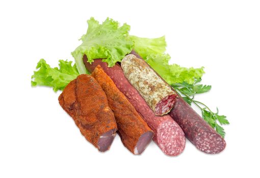 Partly sliced two pieces of the dried pork tenderloin, two different dry smoked sausage and salami with parsley on the lettuce on a light background  
