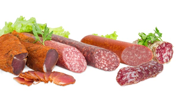 Fragment of the partly sliced two pieces of the dried pork tenderloin, different cooked smoked and dry smoked sausage and salami with parsley twigs and lettuce closeup on a light background  
