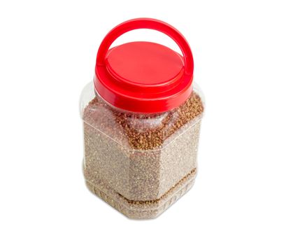 Buckwheat groats peeled from the husk in the transparent plastic container with a red cover on a light background
