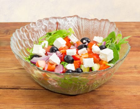 Greek salad in a glass salad bowl on an old wooden surface
