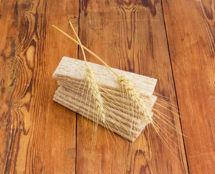 Pile of the dietary wheat wholegrain crispbread with adding a buckwheat and a barley and two wheat spikes on her on an old wooden surface
