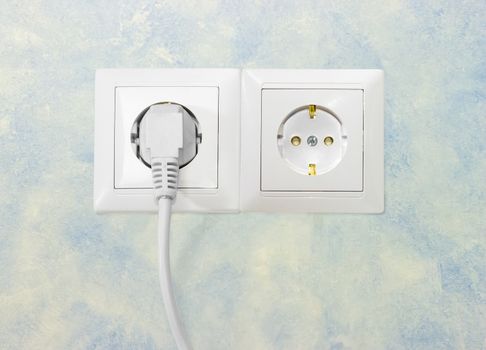 Block of the two white socket outlets European standard with connected one white power cable with corresponding AC power plug closeup on a blue wall

