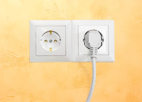 Block of the two white socket outlets European standard with connected one white power cable with corresponding AC power plug closeup on a yellow wall
