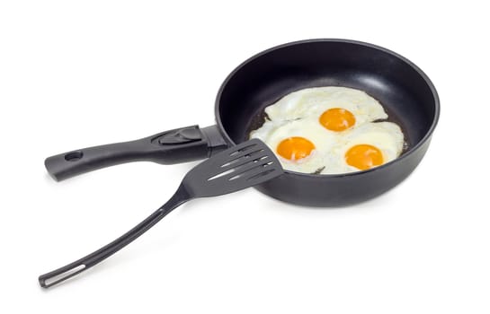 Three freshly fried eggs prepared with unbroken yolk in the frying pan and the black plastic spatula on a light background
