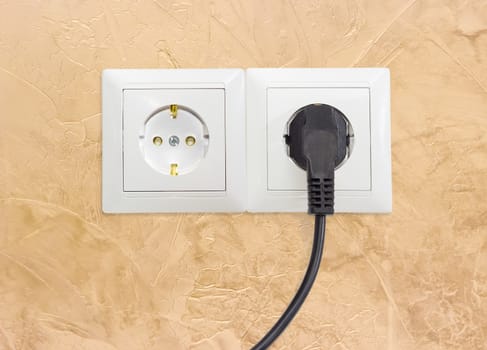 Block of the two white socket outlets European standard with connected one black power cable with corresponding AC power plug closeup on a yellow wall
