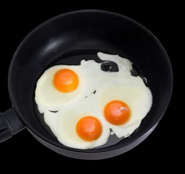 Three fried eggs prepared by sunny side up on the frying pan during cooking closeup on a dark background
