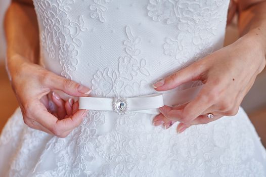 bride adjusts the belt on a white wedding dress in the morning