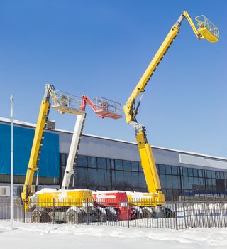 The three different self propelled wheeled hydraulic articulated boom lift with telescoping booms and baskets against the sky and the industrial building in winter sunny day
