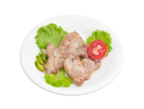 Several slices of fried pork neck on lettuce leaves, sliced green chili and half of tomato on white dish on a light background
