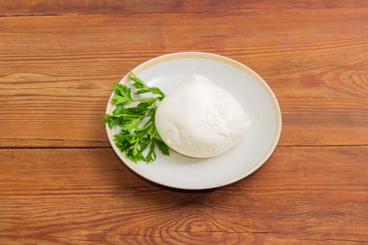 Piece of the fresh mozzarella cheese with twig of parsley on the saucer on an old wooden surface
