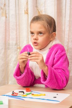 Seven-year girl looked up thoughtfully engaged in modeling of plasticine