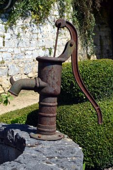 Old metal water pump rest) on the wall of a well.