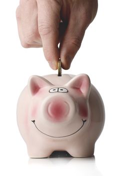 hand placing a coin into smiling piggy bank isolated on a white background