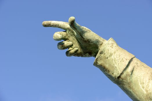 a stone statue hand with finger pointing on a blue sky background 