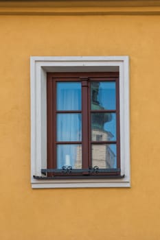 Yellow wall of a house with a window in a white frame. Reflection of a tower of a church and a blue sky. Boskovice, Czech republic.