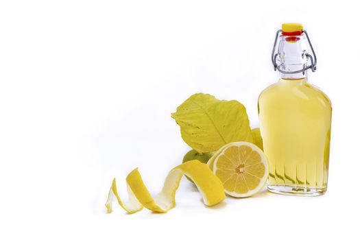 Open glass decanter bottle and shot glass filled with yellow lemon liquor or limoncello or limoncino on white. Peeled natural organic lemon.