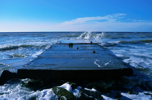 Powerful waves of the sea foam, breaking the concrete pier