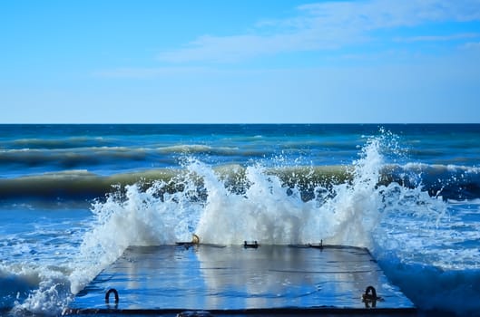 Powerful waves of the sea foam, breaking the concrete pier