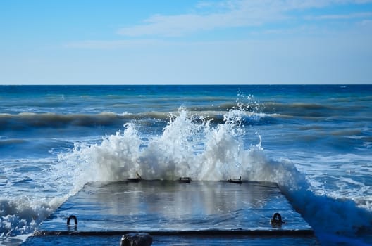 Powerful waves of the sea foam, breaking the concrete pier