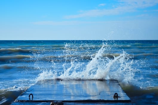 Powerful waves of the sea foam, breaking the concrete pier